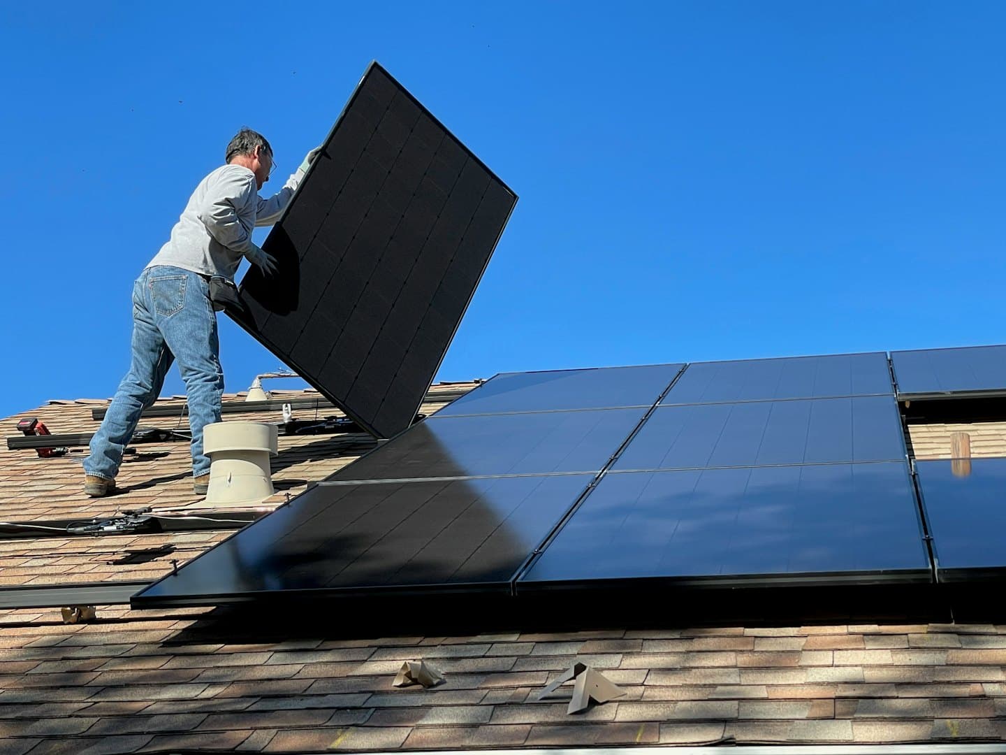 Tecnico installa pannello solare su tetto con scandole sotto cielo azzurro.